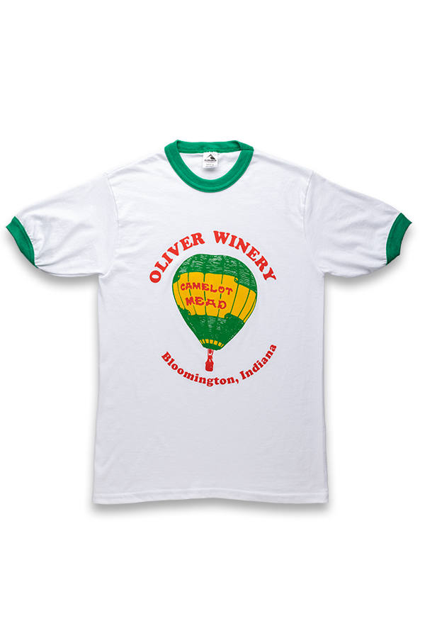 Vintage-style t-shirt in white, with green around neckline and arms. Features an illustration of our Camelot Mead balloon and reads Oliver Winery, Bloomington, IN. 